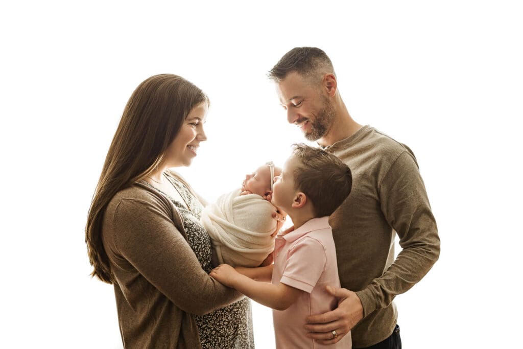 Parents and young sibling smiling at swaddled newborn during in-home newborn session in Cumberland, Rhode Island