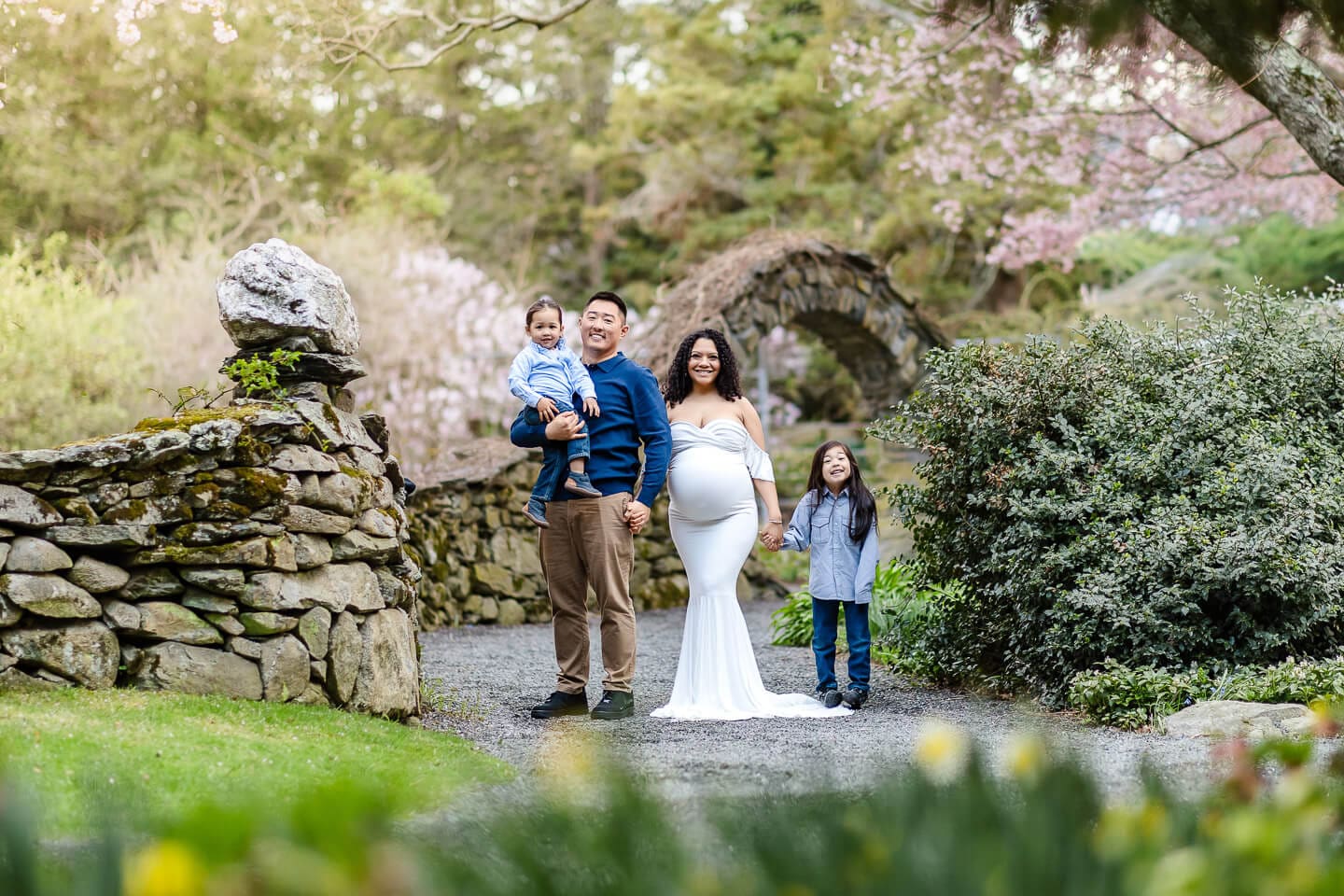 Stone walls and a rustic garden arch frame a growing family during a maternity session in Bristol, Rhode Island.