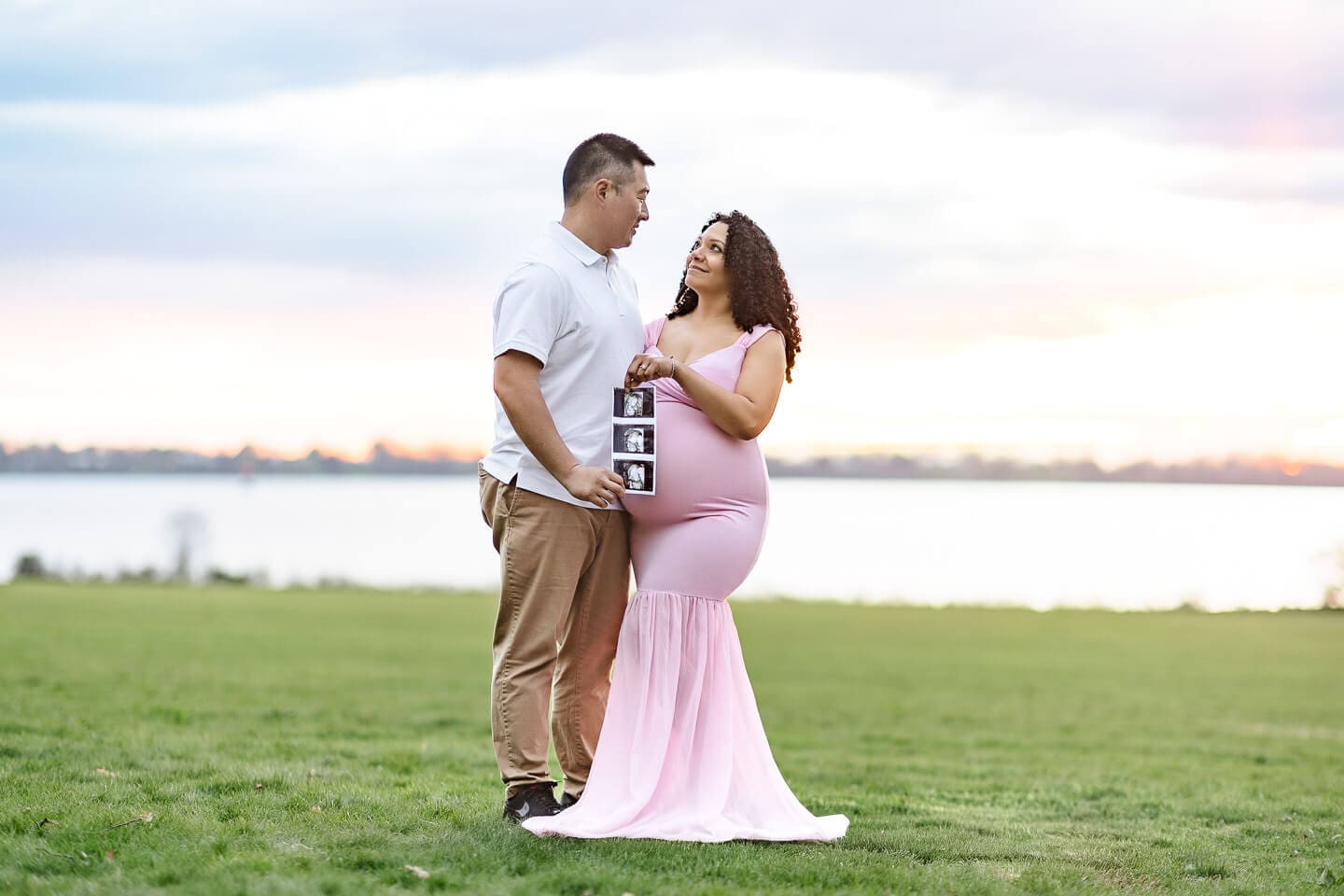 Expecting parents holding ultrasound photos during a maternity photography session by the water in Bristol, Rhode Island.