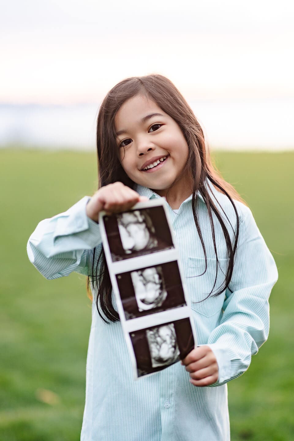 Smiling child holding ultrasound photos during a family maternity photography session in Bristol, Rhode Island.